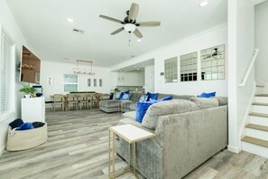 Un salon spacieux avec un canapé gris, une petite table et un ventilateur de plafond.