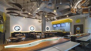 Interior moderno de restaurante com um balcão de madeira comprido, mesas redondas e luminárias pendentes.