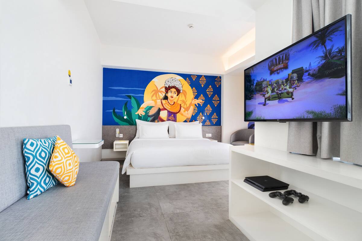 A modern hotel room with a bed, a TV, a sofa, and a wall mural.
