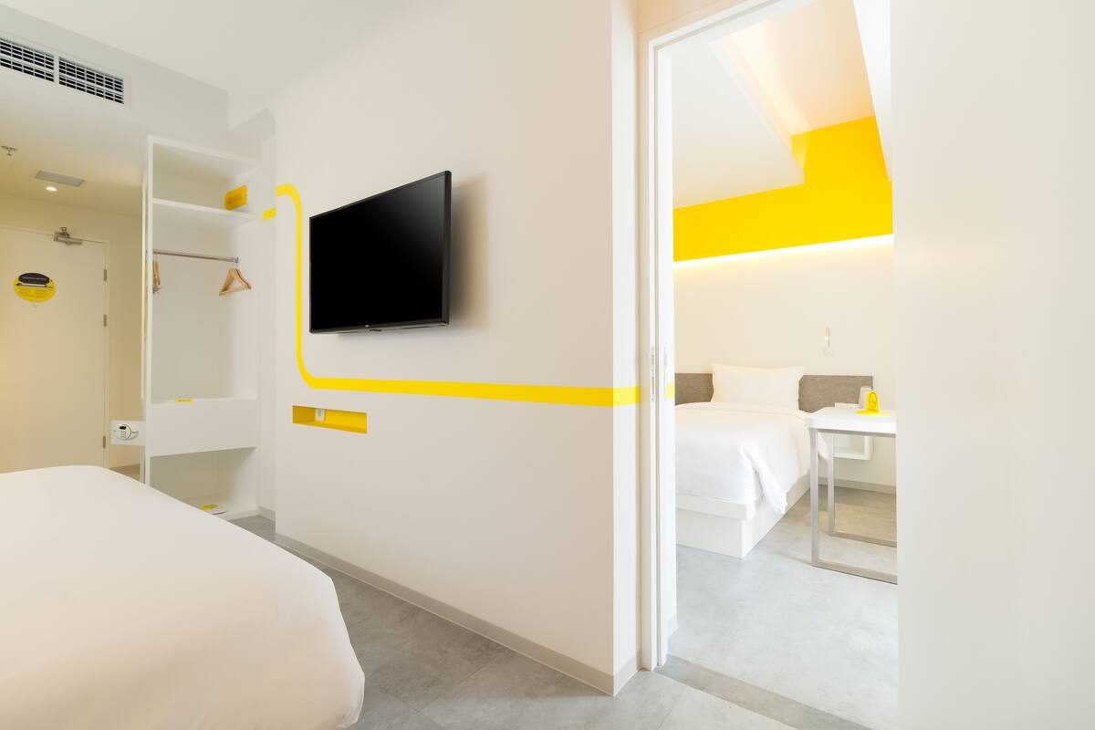 A modern hotel room with a bed, a TV mounted on the wall, a bedside table, and a mirror.
