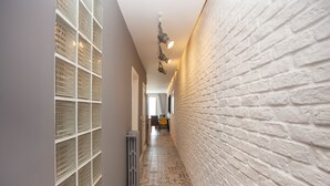 Un couloir étroit avec un sol carrelé, un mur en briques blanches et un radiateur.