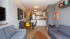 A modern living room with a grey sofa, a dining area with yellow chairs, and a kitchen in the background.