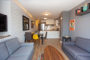 A modern living room with a grey sofa, a dining area with yellow chairs, and a kitchen in the background. - Modern 3BR Apartment · Bosphorus & Dolmabahçe View · Central Beyoğlu (Istanbul)