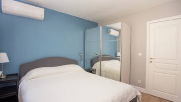 A bedroom with a bed, bedside table, lamp, and a mirror reflecting the room.
