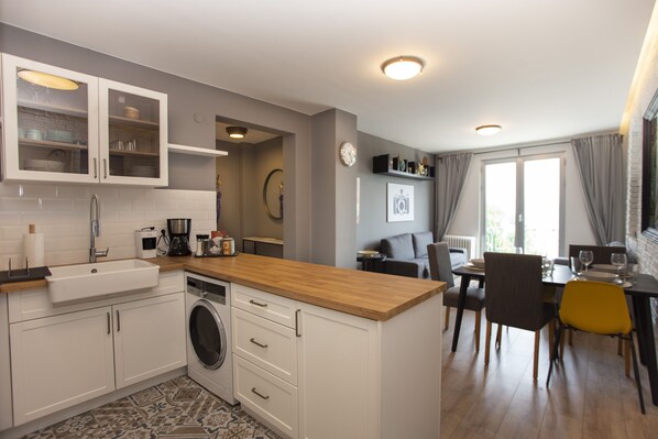 A modern kitchen with a built-in washing machine, a wooden countertop, and a dining area with a table and chairs. - Modern 3BR · Bosphorus View · Central (Istanbul)