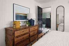Quarto com cama grande, cômoda de madeira, espelho e porta que dá para um banheiro.