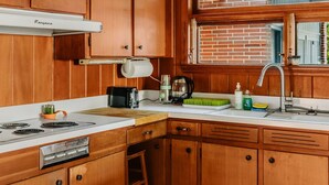 Une cuisine avec des meubles de rangement en bois, une cuisinière à gaz, un évier et une fenêtre donnant sur un immeuble en briques.