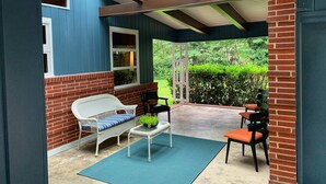 Un patio couvert comprenant un canapé en osier blanc, une petite table avec une plante et deux chaises.