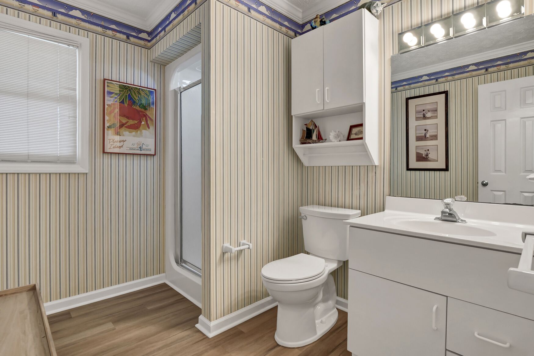 A bathroom with striped wallpaper, a white toilet, a sink with a mirror, and a shower door.