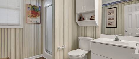 A bathroom with striped wallpaper, a white toilet, a sink with a mirror, and a shower door.