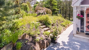 A garden with a stone pathway leading to a white building with a decorative door. - Port Williams Room -KingBed, Patio, Downtown (Wolfville)