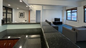 Een moderne woonkamer met een marmeren bar, een grijze bank, een flatscreen televisie en een groot raam.
