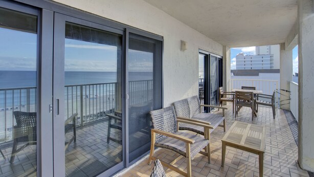 Un balcon avec vue sur la mer, aménagé avec des fauteuils et une table en osier.
