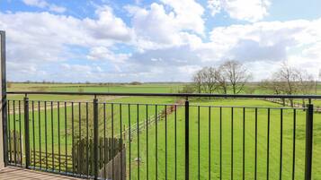 A balcony with a view of a green field and trees.
