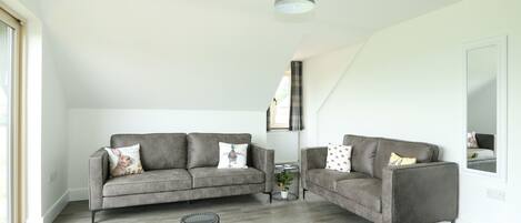 A modern living room with two grey sofas, a small round table with a plant, and a large mirror on the wall.
