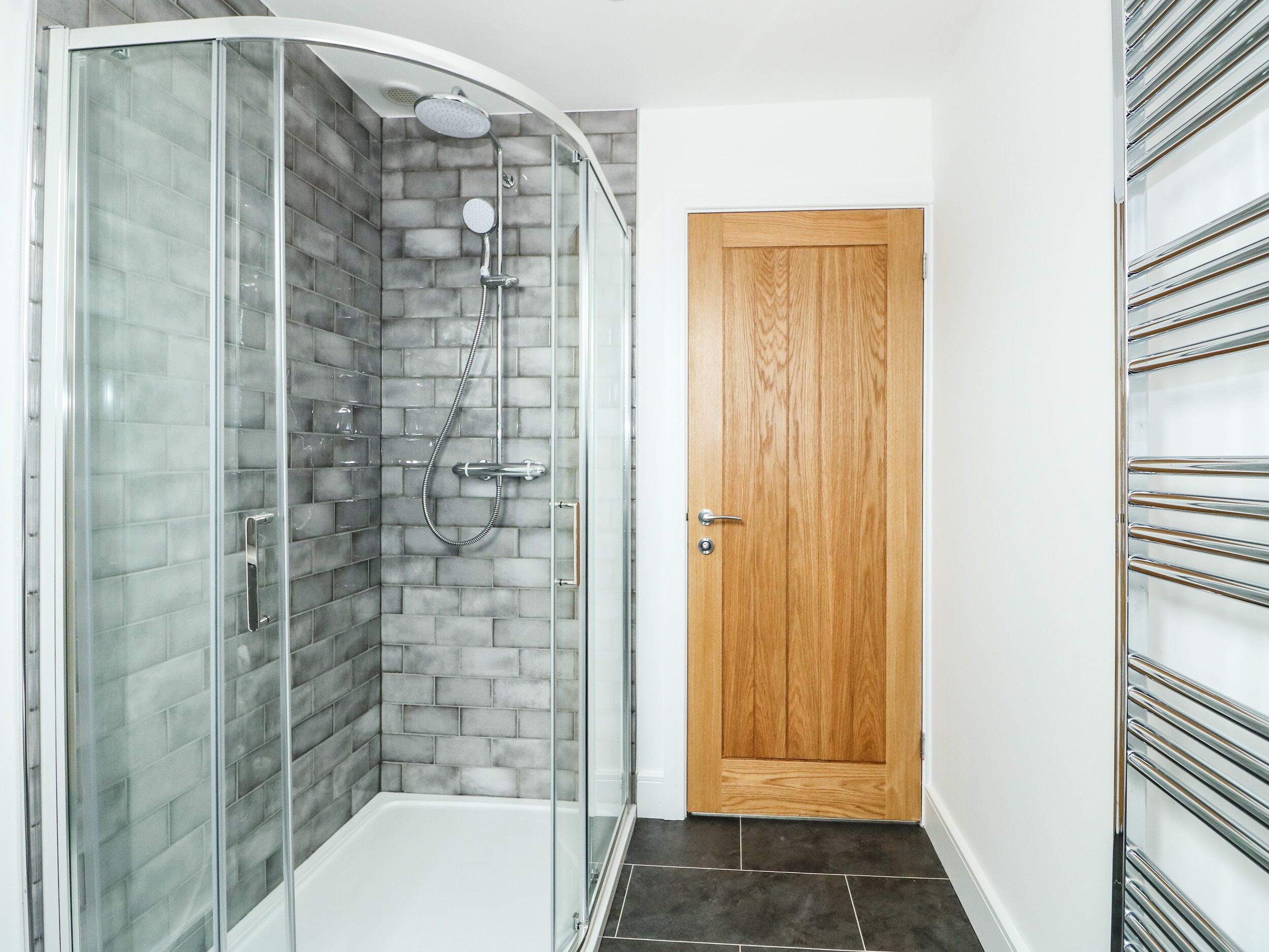 A modern bathroom with a glass shower enclosure, a wooden door, and a tiled floor.