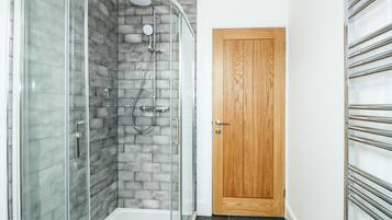 Un baño moderno con cabina de ducha de vidrio, puerta de madera y suelo de baldosas.