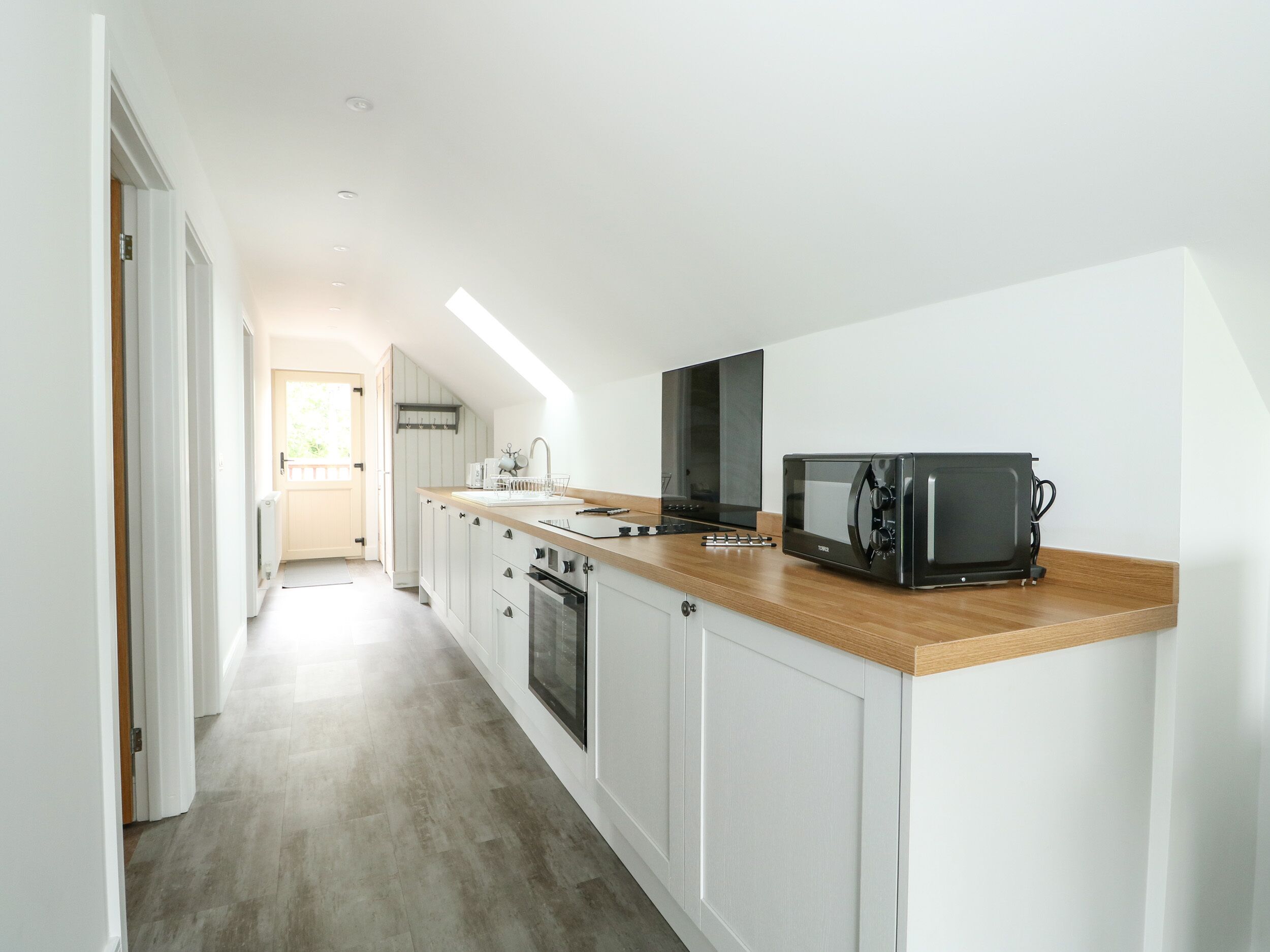 A narrow kitchen with white cabinetry, a wooden countertop, a microwave, and a stove.