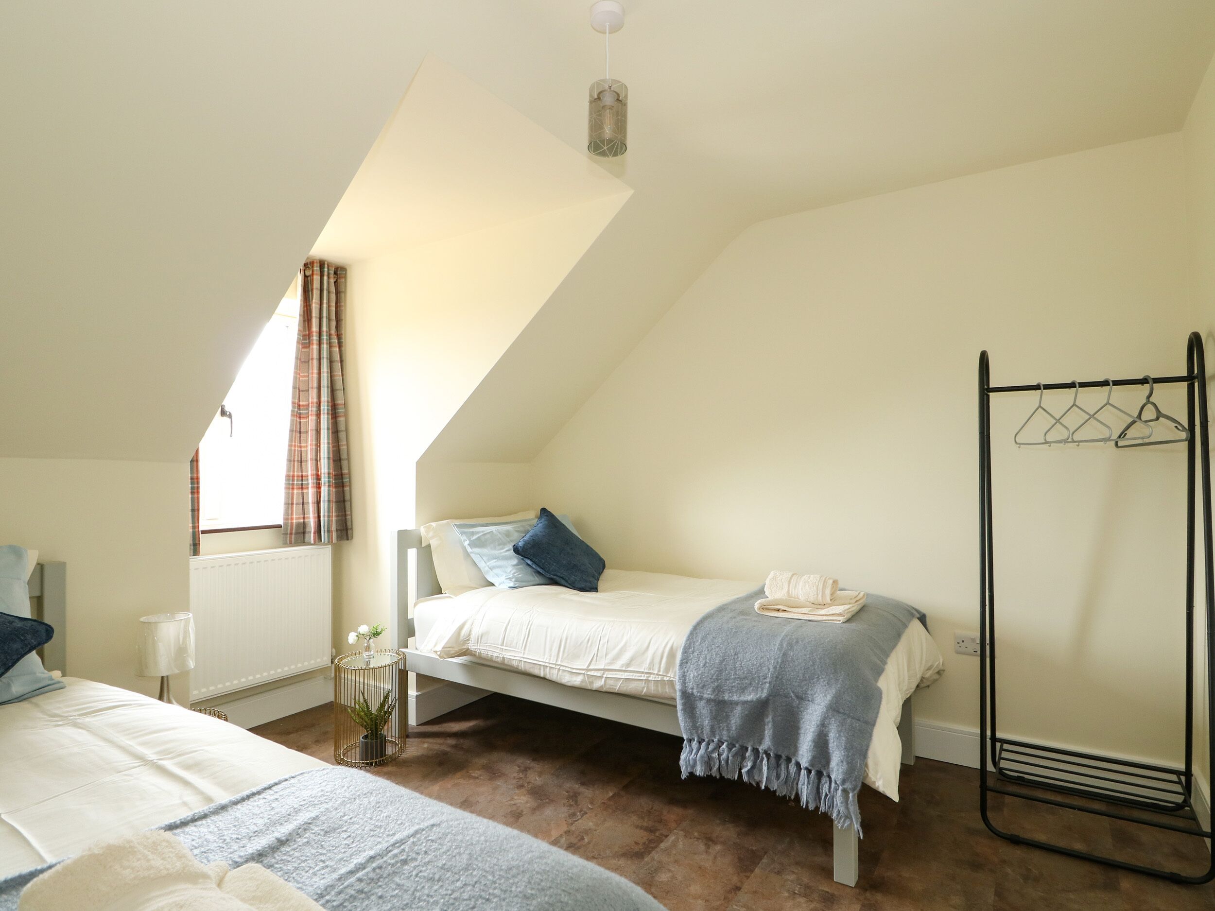 A bedroom with a sloped ceiling, a bed with pillows, a bedside table with a lamp, a radiator, and a window with curtains.