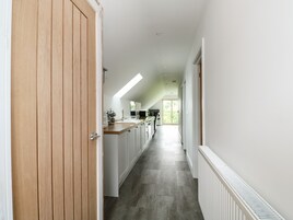 Un pasillo estrecho con una puerta de madera a la izquierda, que da a una zona de cocina con armarios blancos y una encimera.