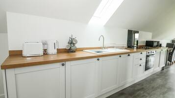 Una cocina moderna con armarios blancos, una encimera de madera, horno empotrado, microondas y cafetera.