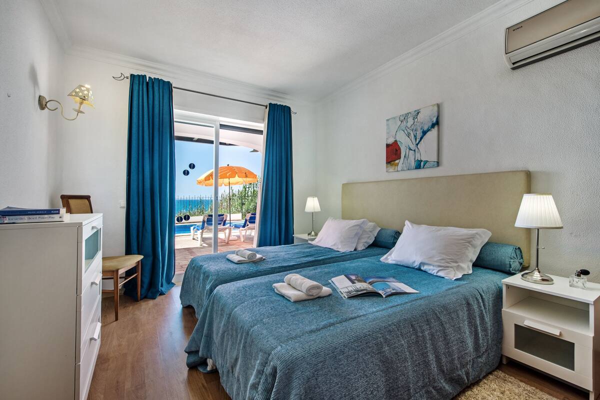 A hotel room with two beds, a desk, a chair, and a view of the pool area.