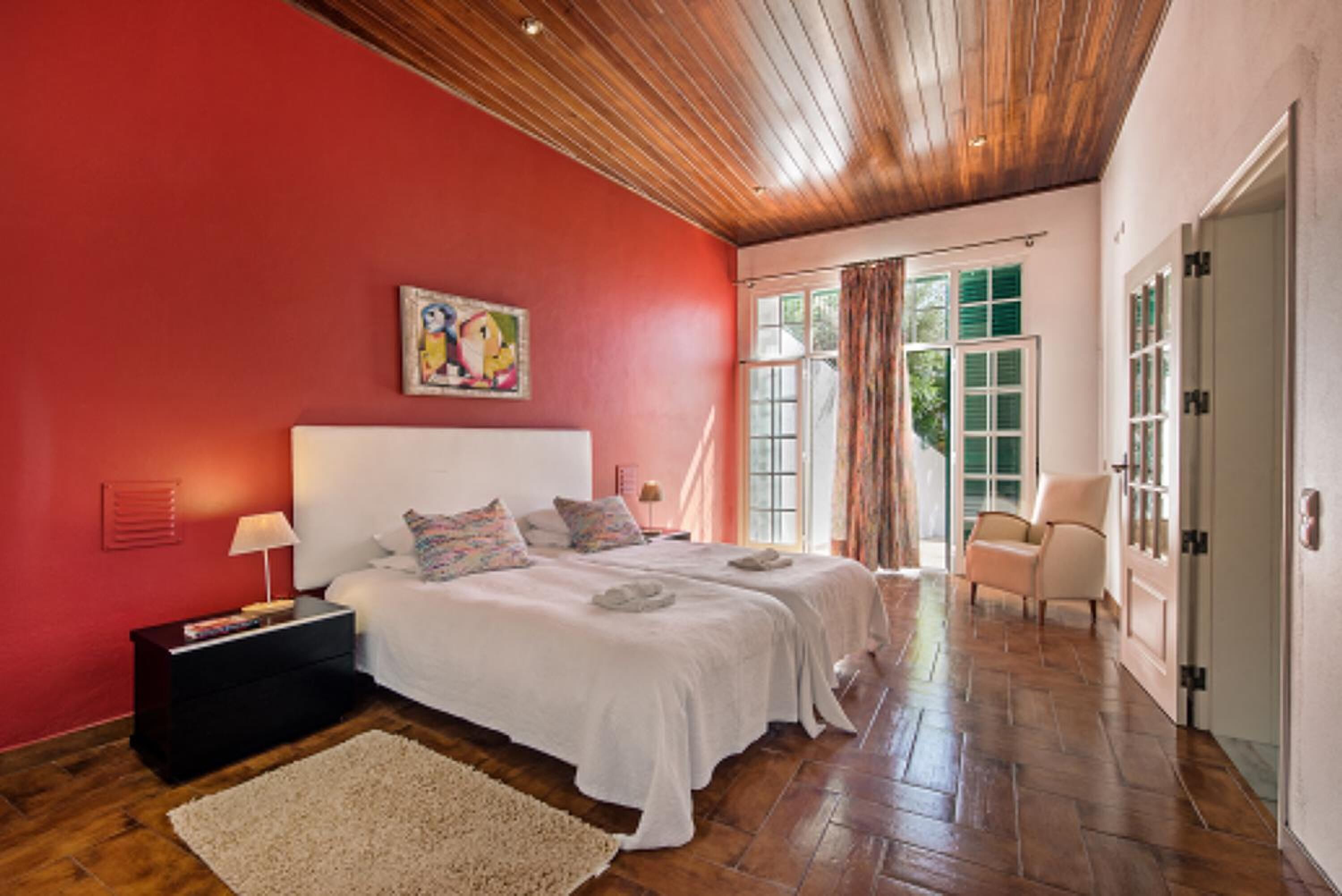 A bedroom with two beds, a wooden ceiling, and a red wall.