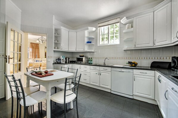 A modern kitchen with white cabinetry, a dining table with chairs, and a window providing natural light. - Forte Sao Joao Villas da Praia (Albufeira)
