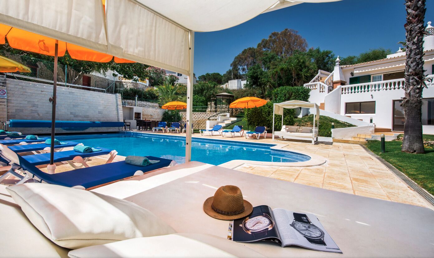 A poolside area with lounge chairs, umbrellas, and a hat on a table.