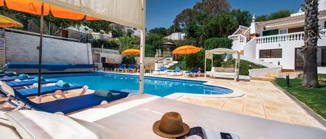 A poolside area with lounge chairs, umbrellas, and a hat on a table.