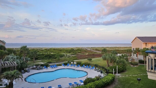 A pool area with blue chairs and a view of the ocean. - Sandy Toes Condo's (Saint Helena Island)