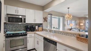 A modern kitchen with stainless steel appliances, a dishwasher, and a large window providing natural light. - Sandy Toes Condo's (Saint Helena Island)