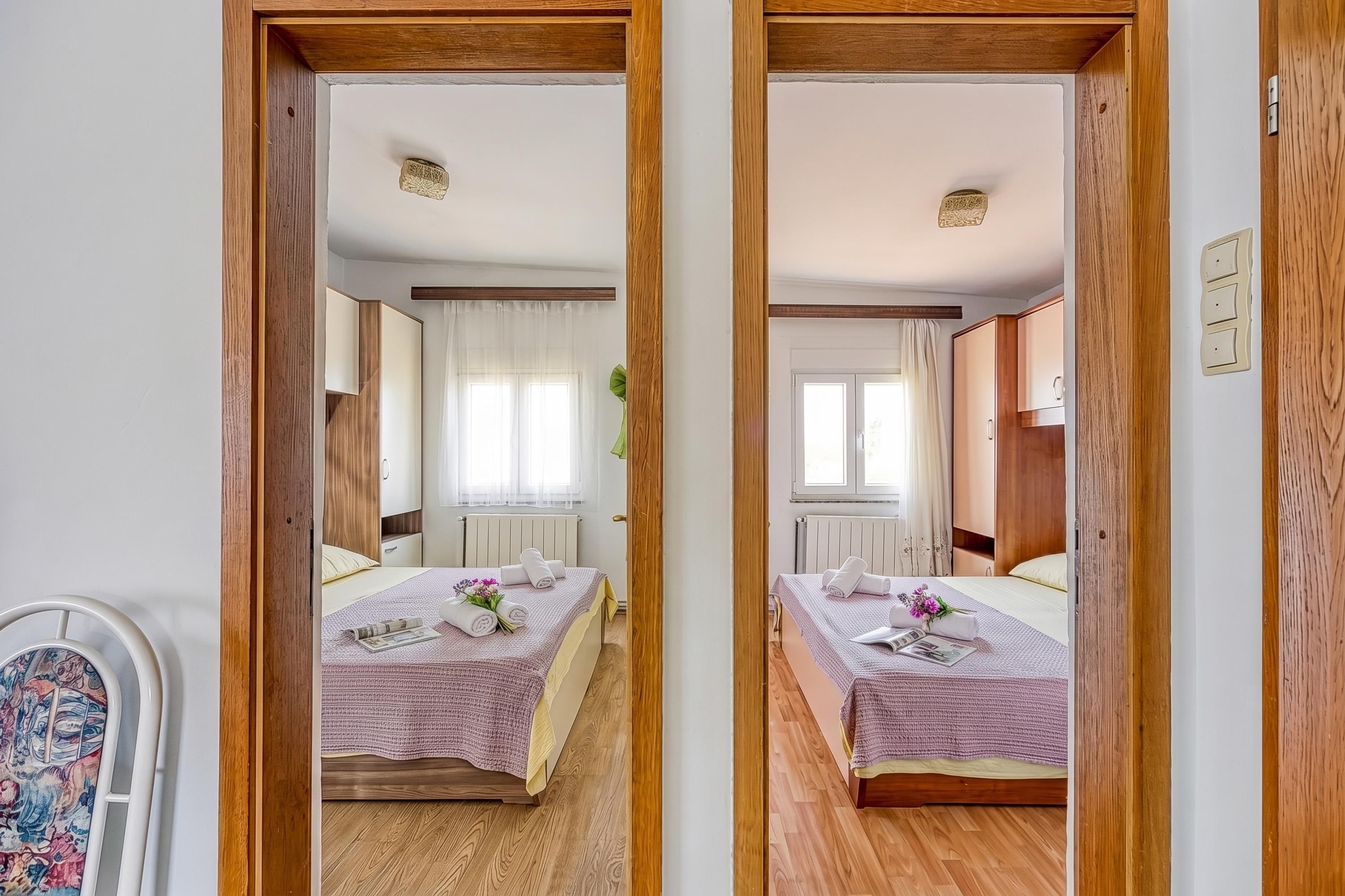 A mirrored view of a hotel room with two beds, wooden flooring, and a window with curtains.