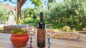 A table with a wine bottle and two wine glasses, a potted plant, and a stone structure in a garden setting. - Vir Island Apartments Basic (Vir)