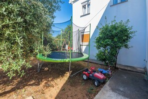 A backyard with a trampoline, a small garden, and a white building.
