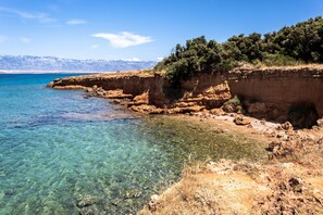 A coastal landscape with clear water, rocky cliffs, and a distant mountain range.