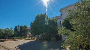 A residential area with a paved driveway, a white building with a balcony, and surrounding greenery. - Vir Island Apartments Basic (Vir)