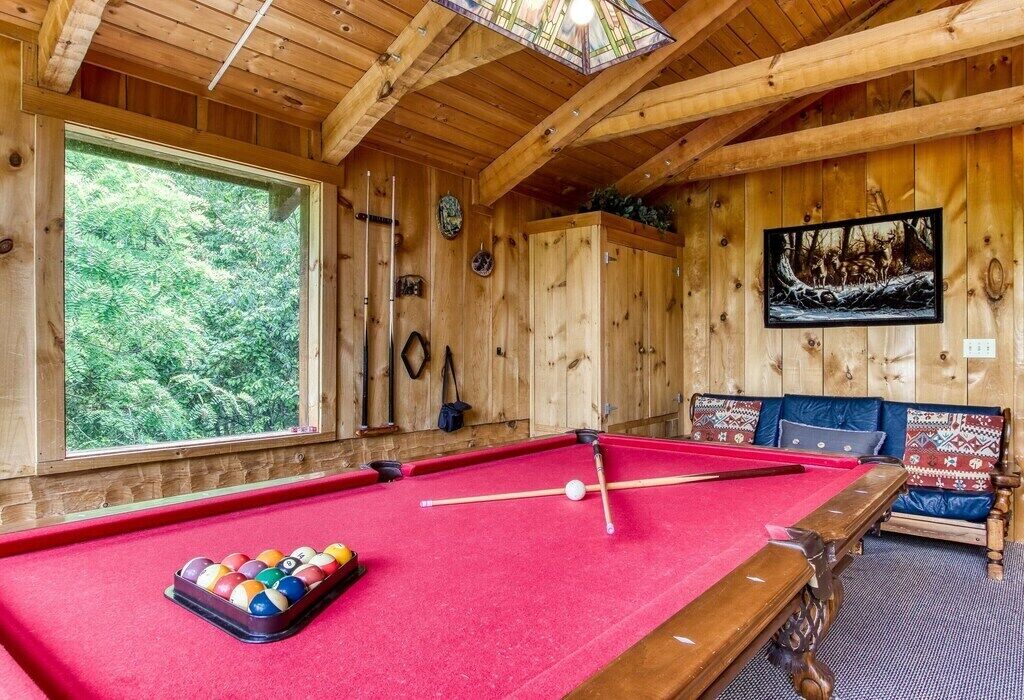 Una habitación de madera con una mesa de billar, un ventanal grande y un cuadro en la pared.