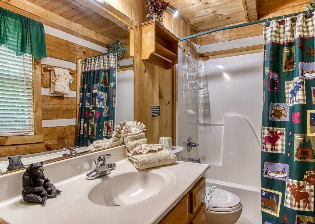 A wooden cabin bathroom with a sink, mirror, towel rack, and a shower with a green curtain.