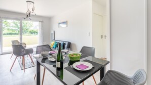 A dining area with a glass table, black chairs, a bottle of wine, and a green basket.