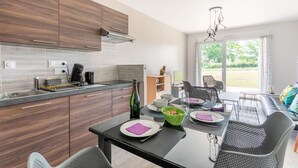 A modern kitchen with wooden cabinets, a dining area with a table set for four, and a large window offering a view of the outdoors.