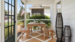 Une terrasse couverte avec une table en bois et des bancs, entourée de panneaux de bardage blancs et dotée d’un sol carrelé.