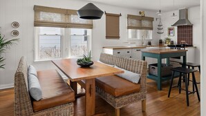 Une cuisine moderne avec une table en bois et des chaises en osier, un poêle et des luminaires suspendus.