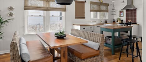 Une cuisine moderne avec une table en bois et des chaises en osier, un poêle et des luminaires suspendus.