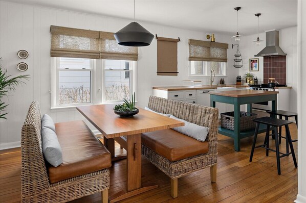 Una cocina moderna con una mesa de madera y sillas de mimbre, una estufa y luces colgantes.