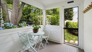 Une véranda abritée avec une table et des chaises, une plante en pot et une vue sur la verdure environnante.