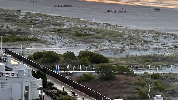 Ein Küstenblick mit Sonnenuntergang, Strand und einem Gebäude mit Balkon mit Blick auf den Strand.