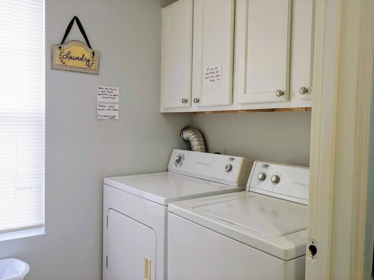A laundry room with two white washers and dryers, a hanging laundry sign, and a note on the wall.