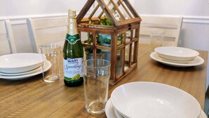 A dining table with white plates, a bottle of Sparkling White Grape wine, and a clear glass. A wooden lantern with a glass enclosure is also visible. - Cliffside Cottage 4 - Near SDC, Lake, & Downtown! (Branson)
