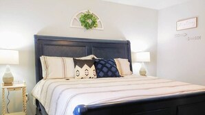 A neatly made bed with a dark headboard, two bedside tables with lamps, and a wall-mounted sign. - Cliffside Cottage 4 - Near SDC, Lake, & Downtown! (Branson)